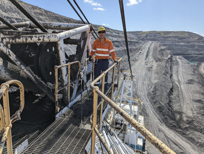 An engineer in high-visibility workwear on mining equipment overlooking an open-cut mine.
